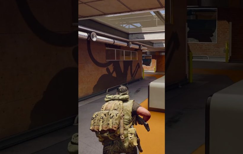 Soldier with large backpack and rifle crouching in industrial corridor under skylights