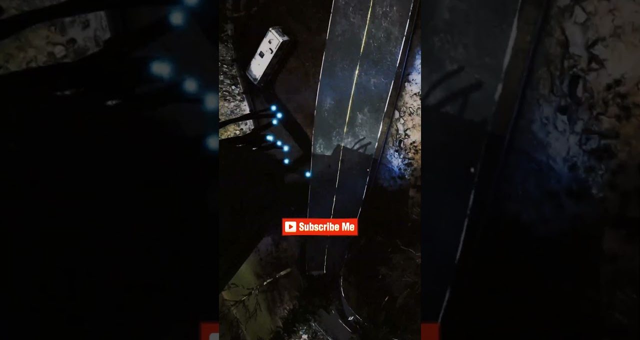 Dark nighttime aerial view of a narrow road with a parked white van and glowing blue lights