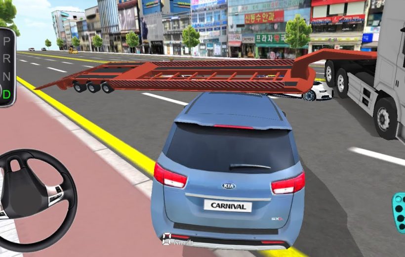 Blue Kia Carnival stopped behind a low car transporter trailer across city street.