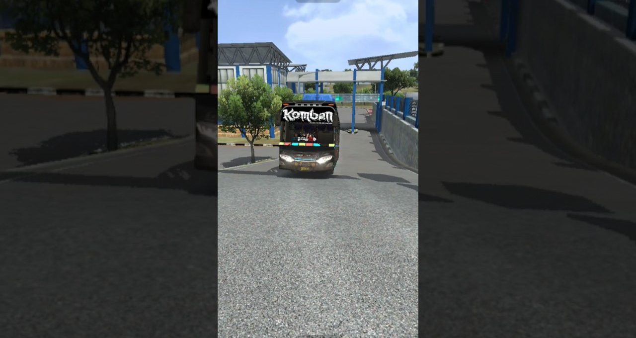 Black coach bus labeled "Komban" driving up a paved road near station.