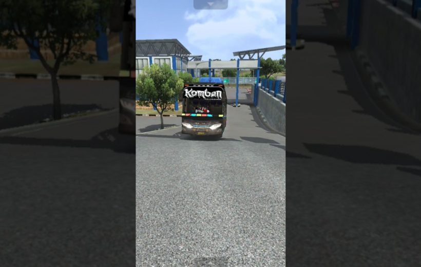 Black coach bus labeled "Komban" driving up a paved road near station.