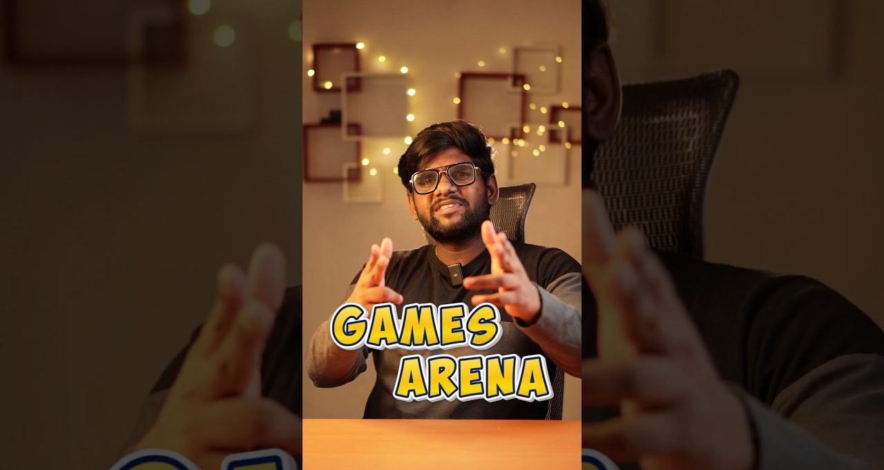 Man speaking enthusiastically at desk with "Games Arena" text and warm string lights