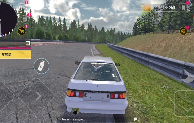 White hatchback racing car parked beside a racetrack barrier with forested backdrop
