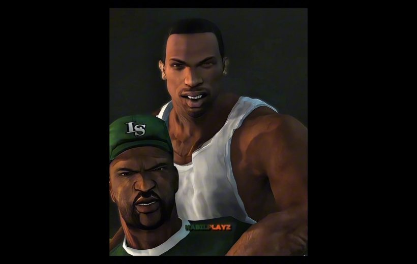 Two muscular men pose together, one in a white tank top and one wearing a green cap.