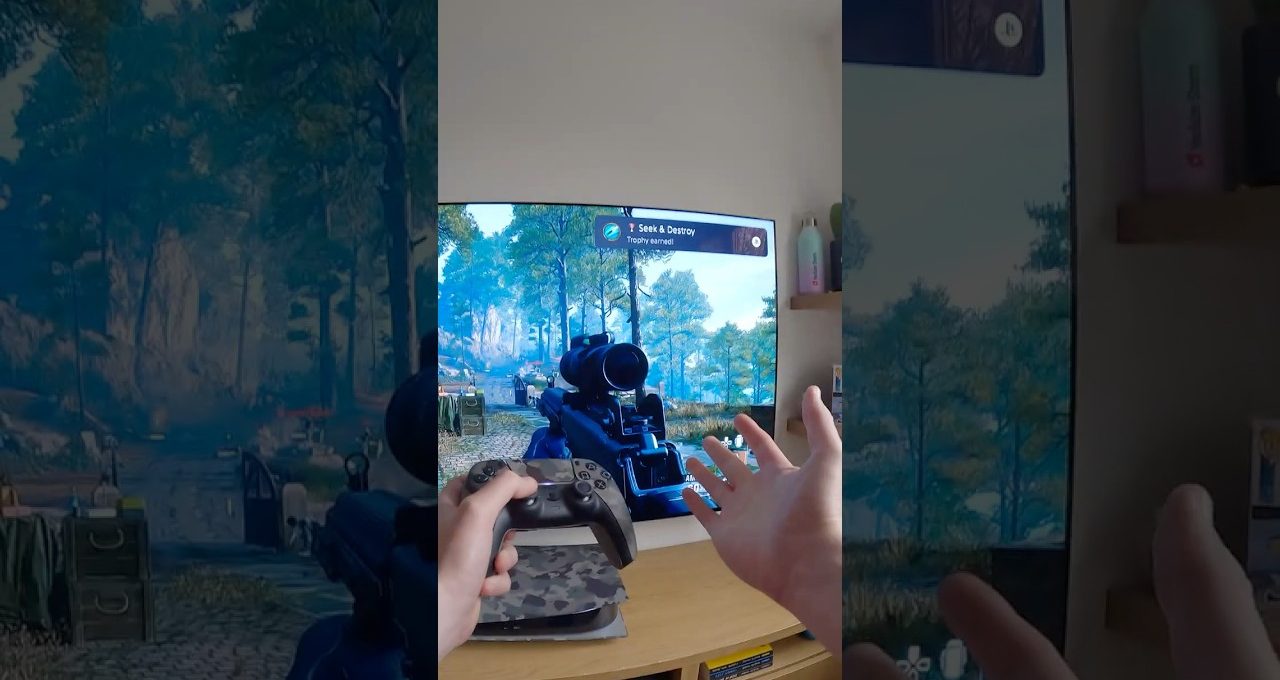 Person holding a game controller playing a first-person shooter on TV screen