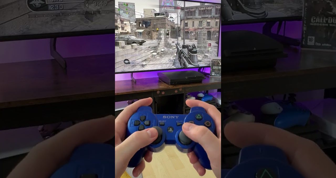 Hands holding a blue Sony controller playing a first-person shooter on TV