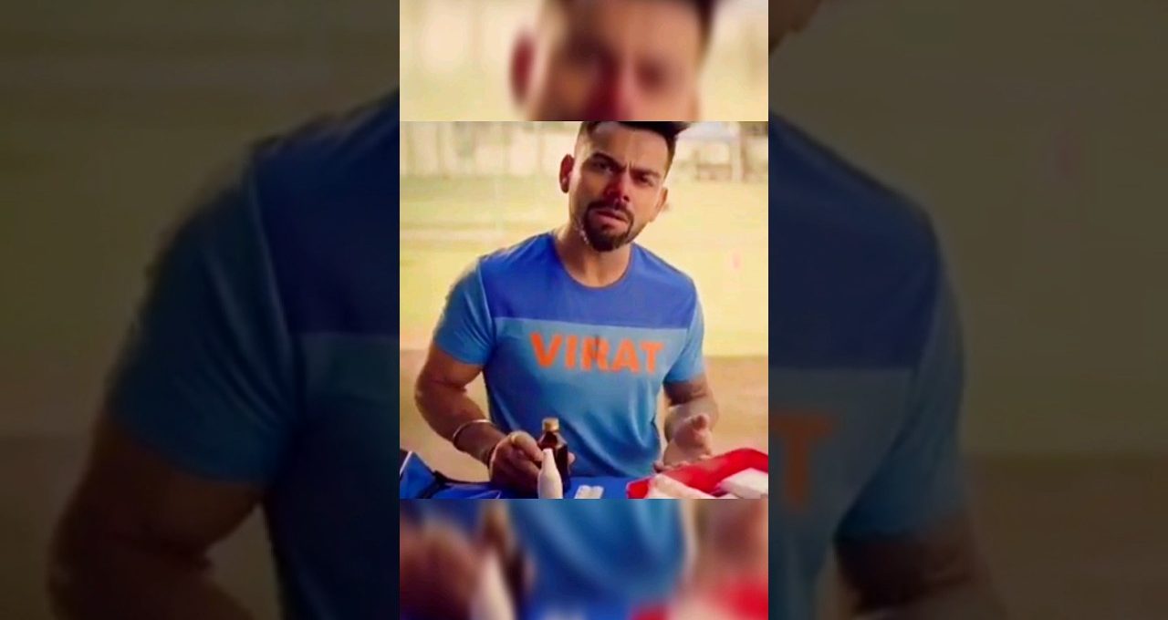 Man in blue t-shirt labeled "VIRAT" gesturing while holding a bottle at a table