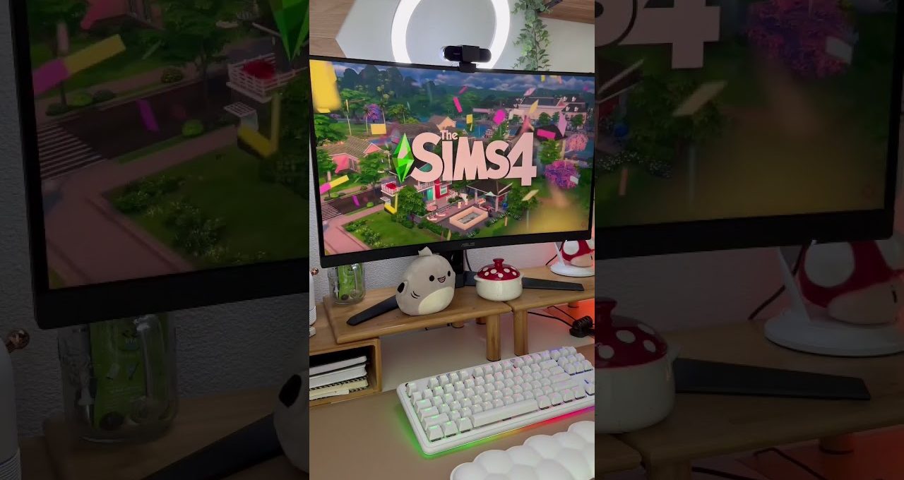 Gaming desk setup with The Sims 4 on monitor, keyboard, plush and mushroom decor