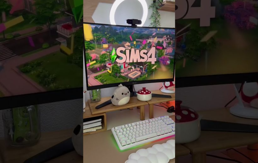Gaming desk setup with The Sims 4 on monitor, keyboard, plush and mushroom decor