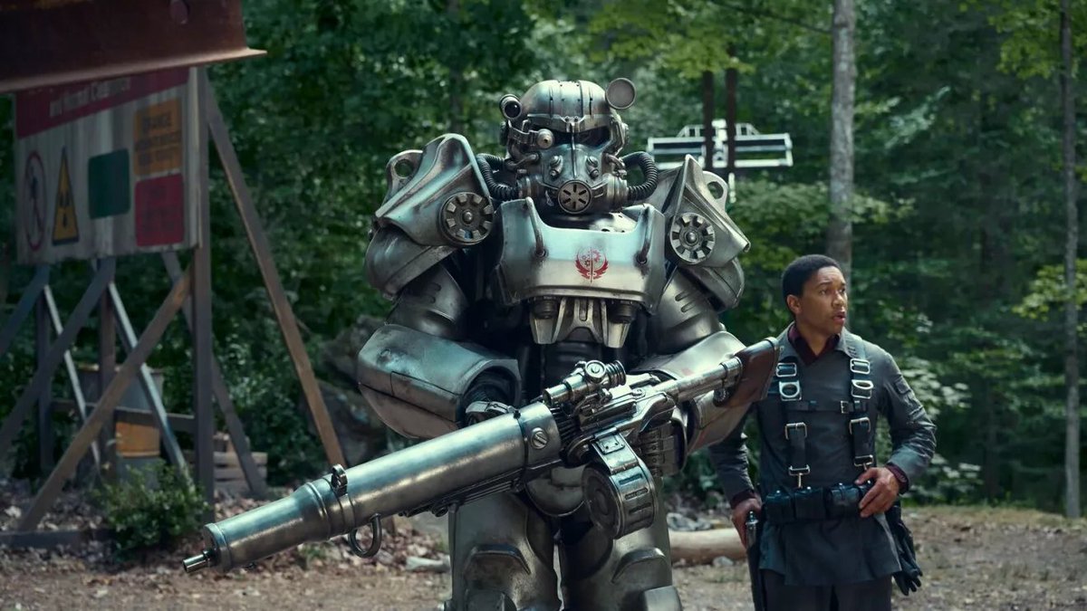 Armored power-suit soldier holding a large rifle beside a man in harnessed uniform