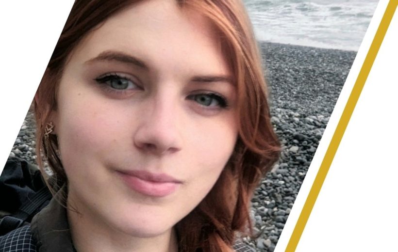 Young woman with red hair smiling on a rocky beach, overlaid with a mentorship name banner.
