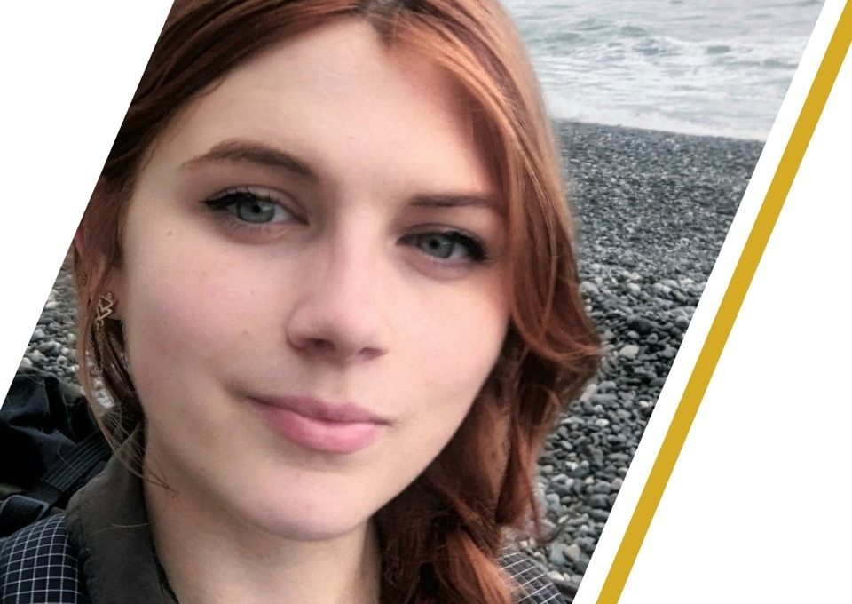 Young woman with red hair smiling on a rocky beach, overlaid with a mentorship name banner.