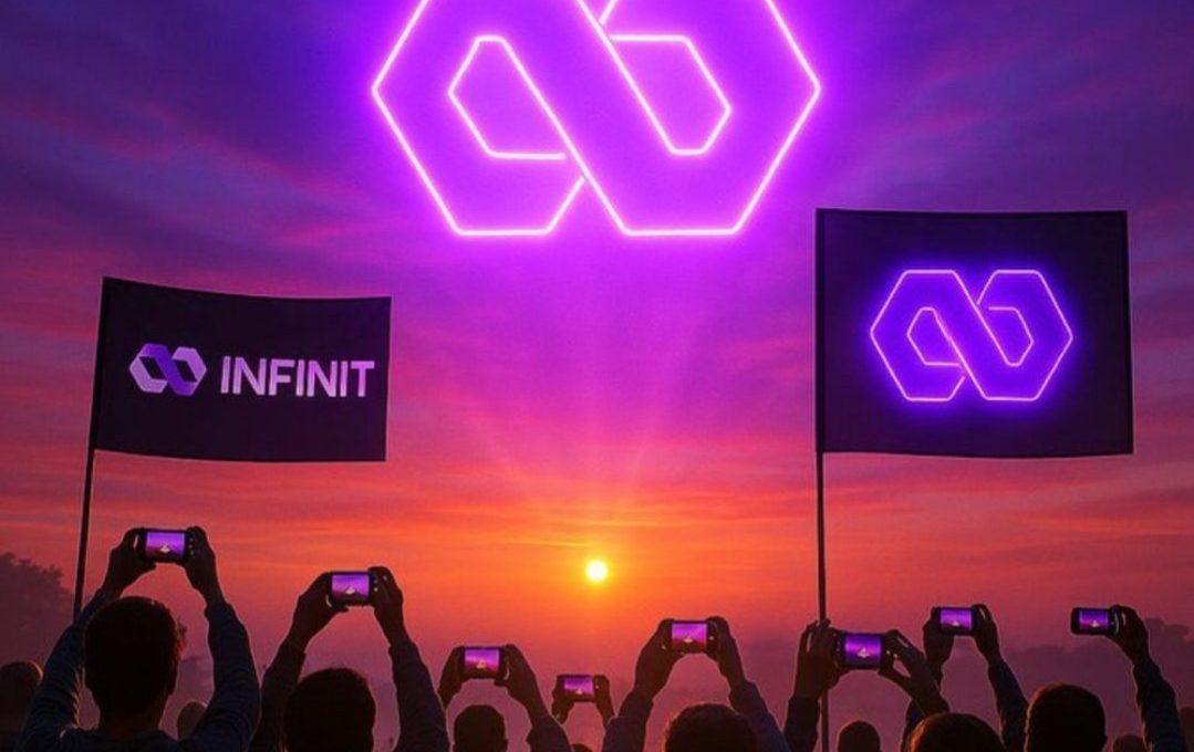 Silhouetted crowd holding phones at sunset watching large glowing neon infinity logo flags.