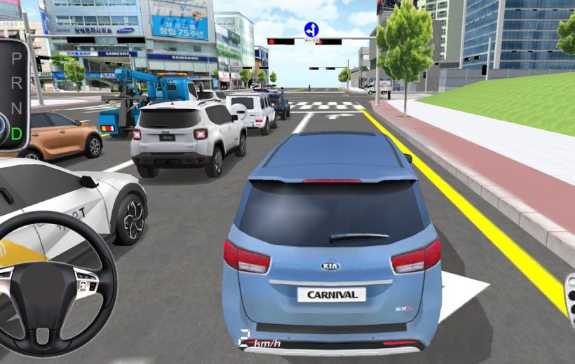 Blue Kia Carnival minivan driving in traffic toward an urban intersection with buildings