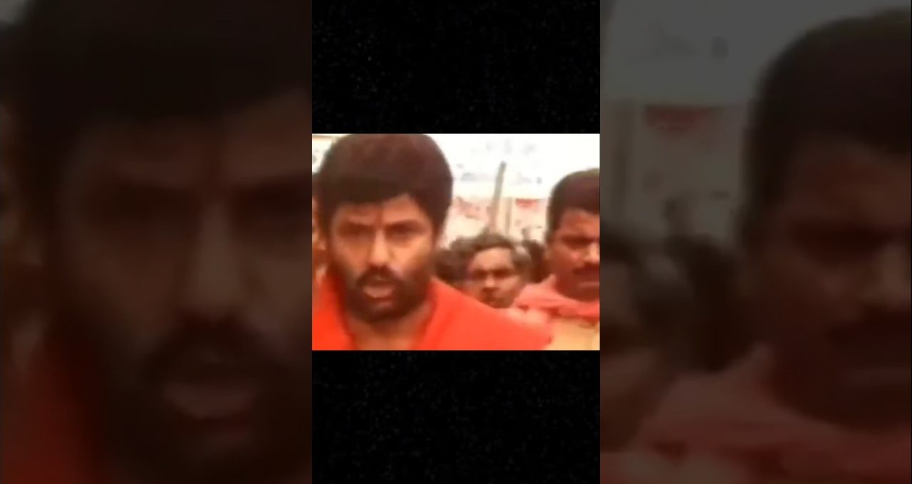 Bearded man in orange clothing leading a crowd of people outdoors during procession