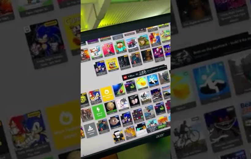 Desktop monitor displaying a grid of colorful game thumbnails and app icons on screen