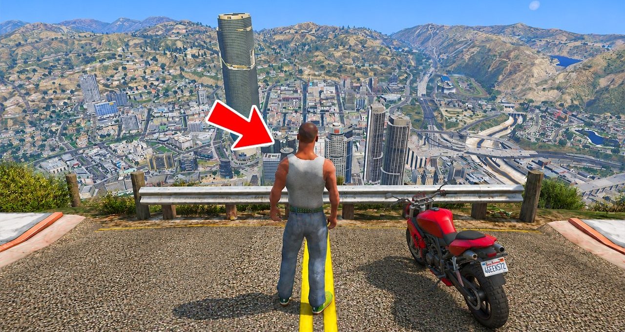 Man in tank top and jeans standing at cliff overlooking city with parked motorcycle