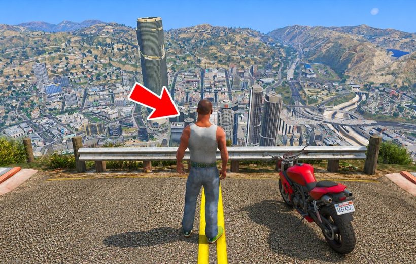 Man in tank top and jeans standing at cliff overlooking city with parked motorcycle
