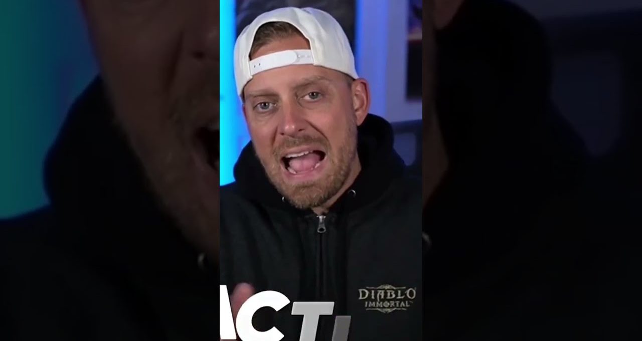Man wearing backwards white cap and Diablo Immortal hoodie speaking to camera indoors
