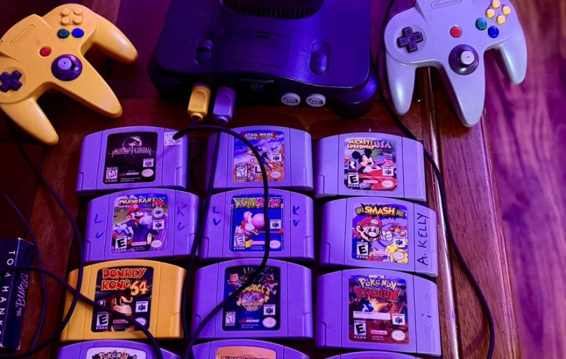 Nintendo 64 console with two controllers and a grid of game cartridges on table