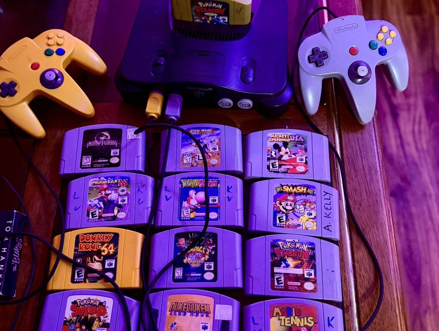 Nintendo 64 console with two controllers and a grid of game cartridges on table