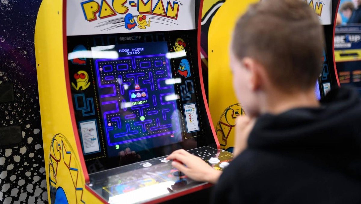 Child playing a classic Pac-Man arcade cabinet, focused on the glowing maze screen