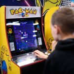 Child playing a classic Pac-Man arcade cabinet, focused on the glowing maze screen