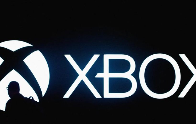Silhouetted person walking past a large illuminated Xbox logo and wordmark on black background
