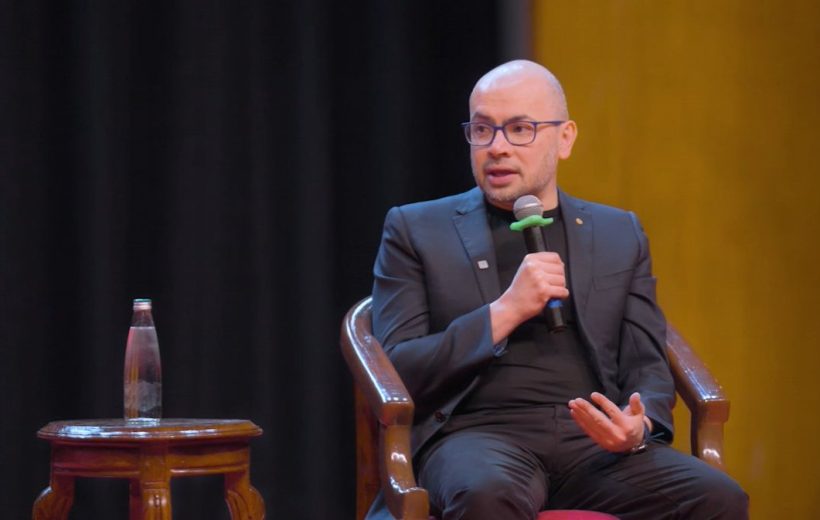 Bald man wearing glasses and suit speaking into a microphone during a panel discussion