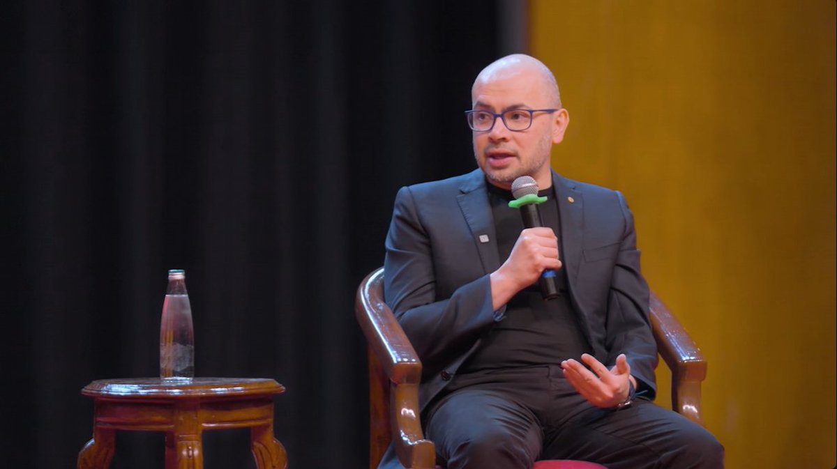 Bald man wearing glasses and suit speaking into a microphone during a panel discussion